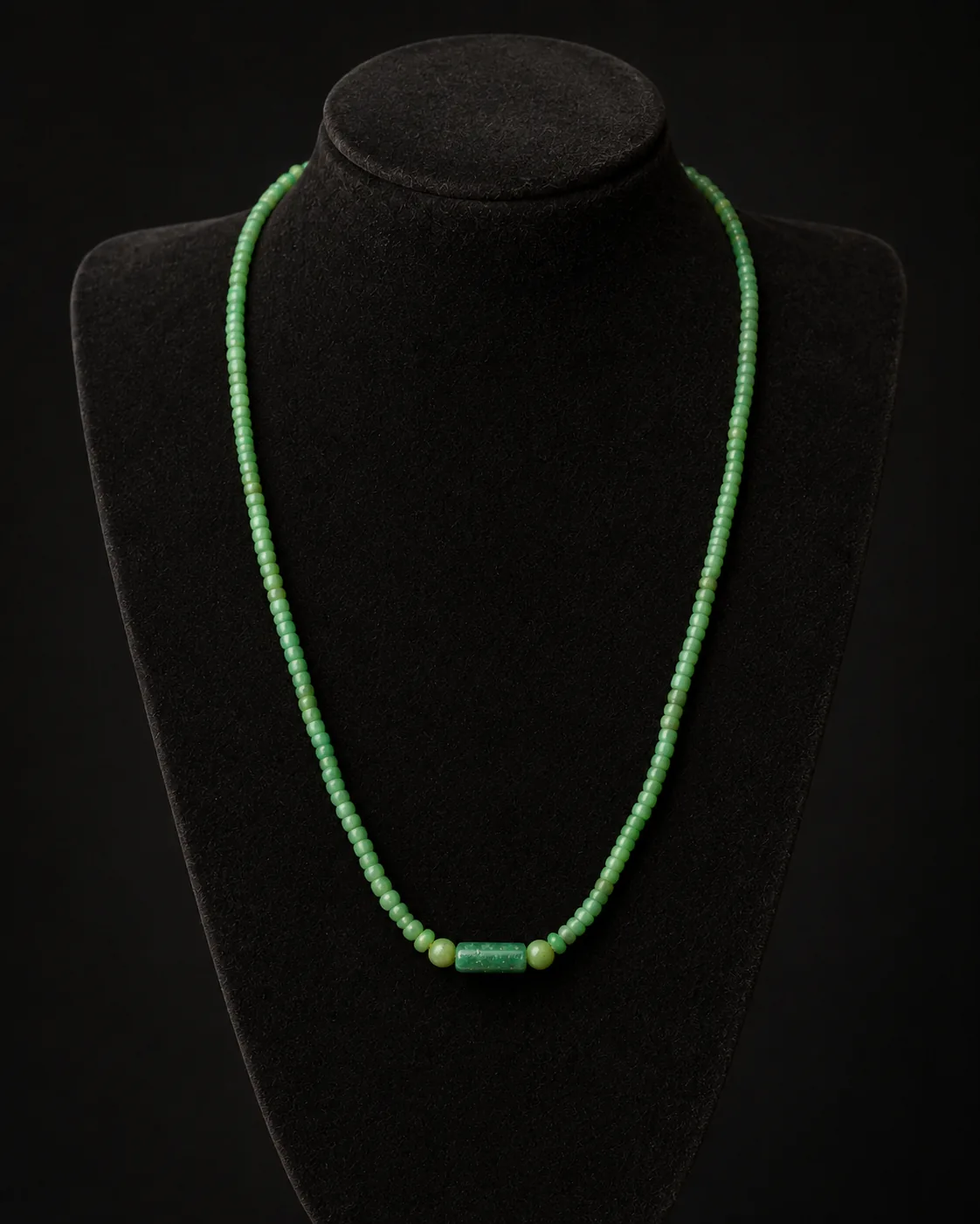 Collar romano de cuentas de vidrio verde sobre un busto de museo en gris carbón